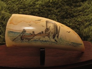 Scrimshaw on whale tooth by Philip Hoyte depicting a skiff with whalers and a sperm whale breaching the water beside them.