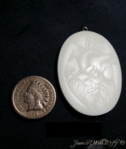 Coin next to a scrimshawed cabochon of a human heart not colored in.