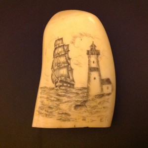 Rounded whale tooth with a ship and a lighthouse scrimshawed on the one side.