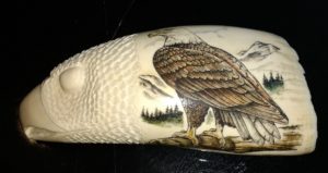 Scrimshaw carving of an eagle's head facing left, with a full color eagle scrimshawed on the neck.