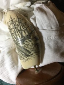 Whale tooth scrimshaw of a whale in the foreground with a ship in the background, signed "Rudy"